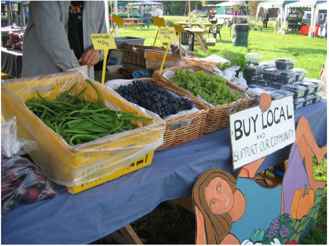 Buy local food sign at farmers market stall displaying homegrown grapes berries and veges