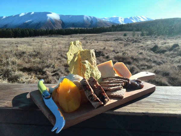 Delicious artisan cheese platter served on wooden board with scenic snow capped mountains in background